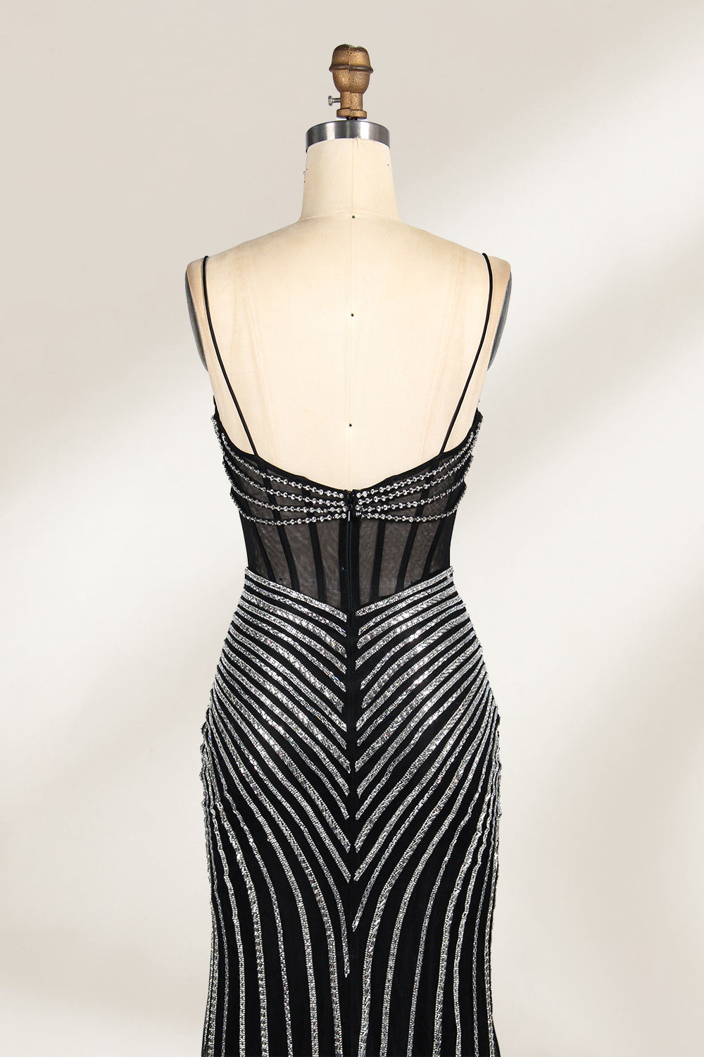 A mannequin showcases a black gown with silver beading. It has thin straps, a sheer bodice, and a high side slit. The geometric beading pattern adds glamour, making it perfect for formal events like galas or proms, radiating sophistication.4