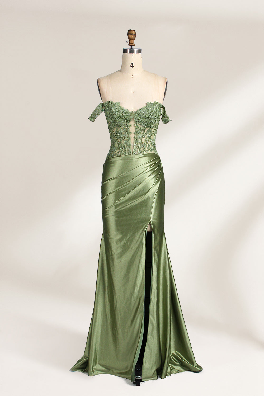 A mannequin showcases an olive - green gown. It has off - the - shoulder, lace - detailed sleeves, a sheer bodice with floral embroidery, and a high side slit. The elegant design, blending satin and lace, suits formal events like galas, radiating charm.1