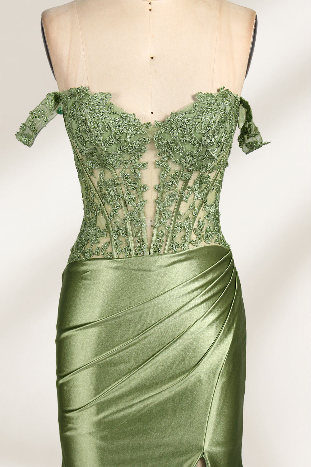 A mannequin showcases an olive - green gown. It has off - the - shoulder, lace - detailed sleeves, a sheer bodice with floral embroidery, and a high side slit. The elegant design, blending satin and lace, suits formal events like galas, radiating charm.5