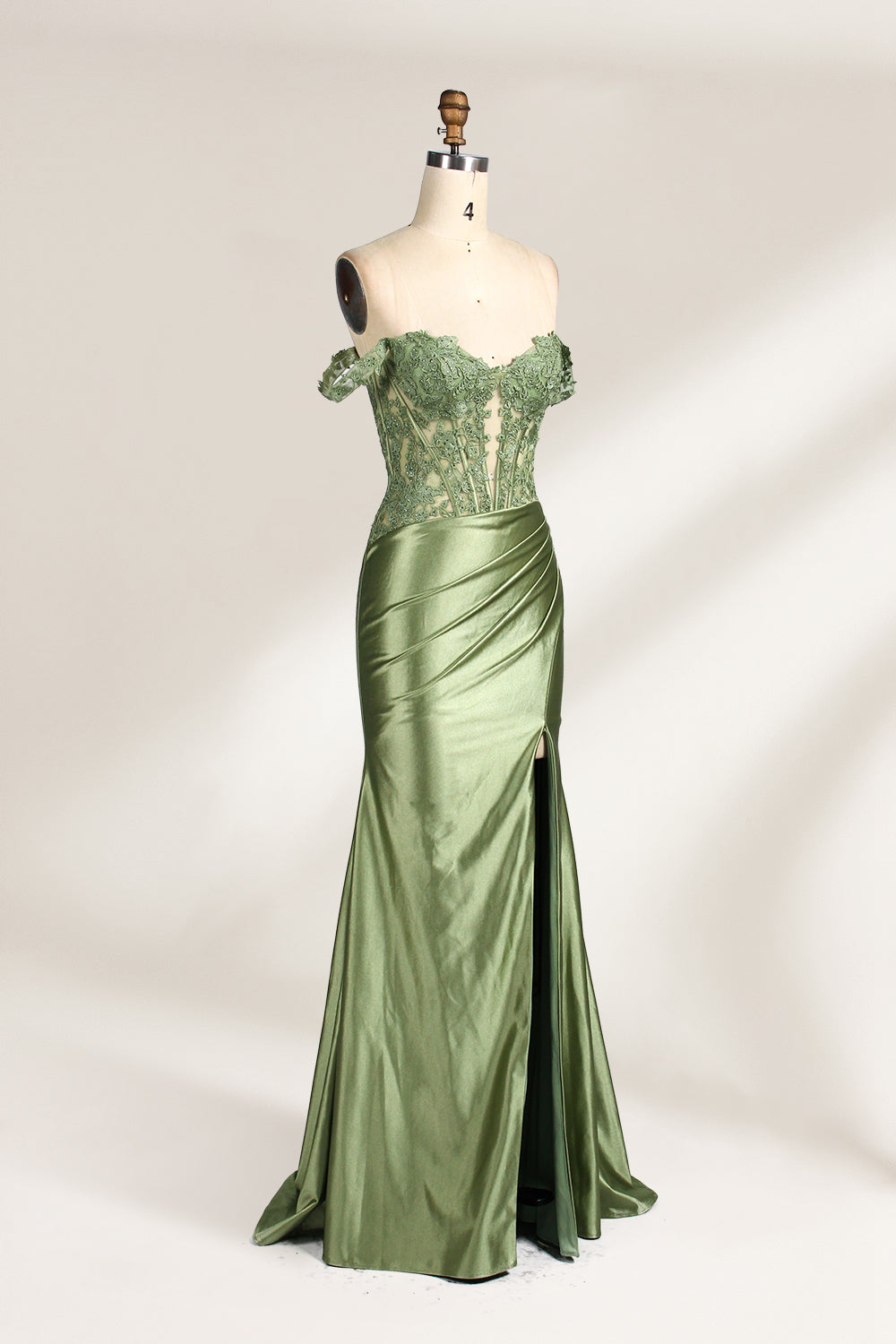 A mannequin showcases an olive - green gown. It has off - the - shoulder, lace - detailed sleeves, a sheer bodice with floral embroidery, and a high side slit. The elegant design, blending satin and lace, suits formal events like galas, radiating charm.3