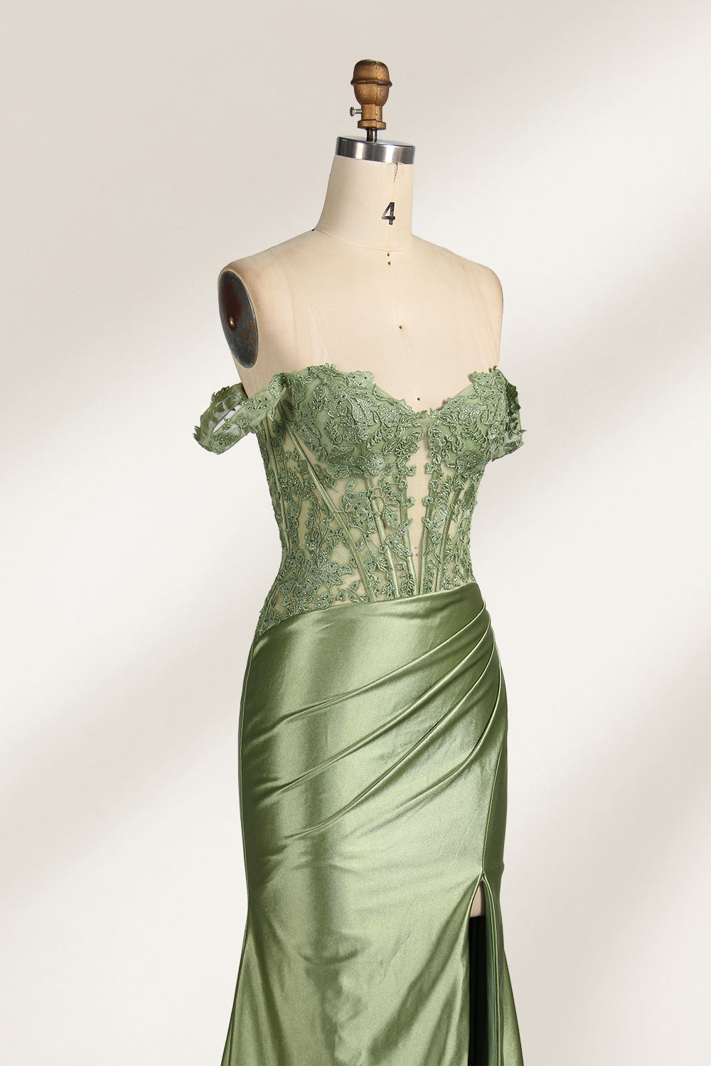 A mannequin showcases an olive - green gown. It has off - the - shoulder, lace - detailed sleeves, a sheer bodice with floral embroidery, and a high side slit. The elegant design, blending satin and lace, suits formal events like galas, radiating charm.6