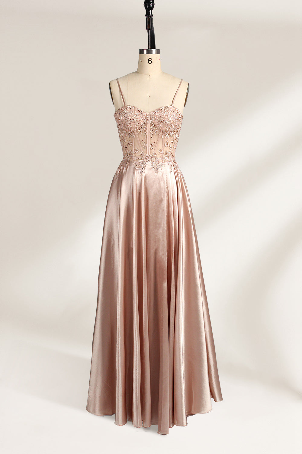 A mannequin showcases a champagne - satin gown. It has thin straps, a sheer lace - detailed bodice, and a voluminous skirt. The elegant design, blending satin and intricate lace, suits formal events like weddings, radiating sophistication.1