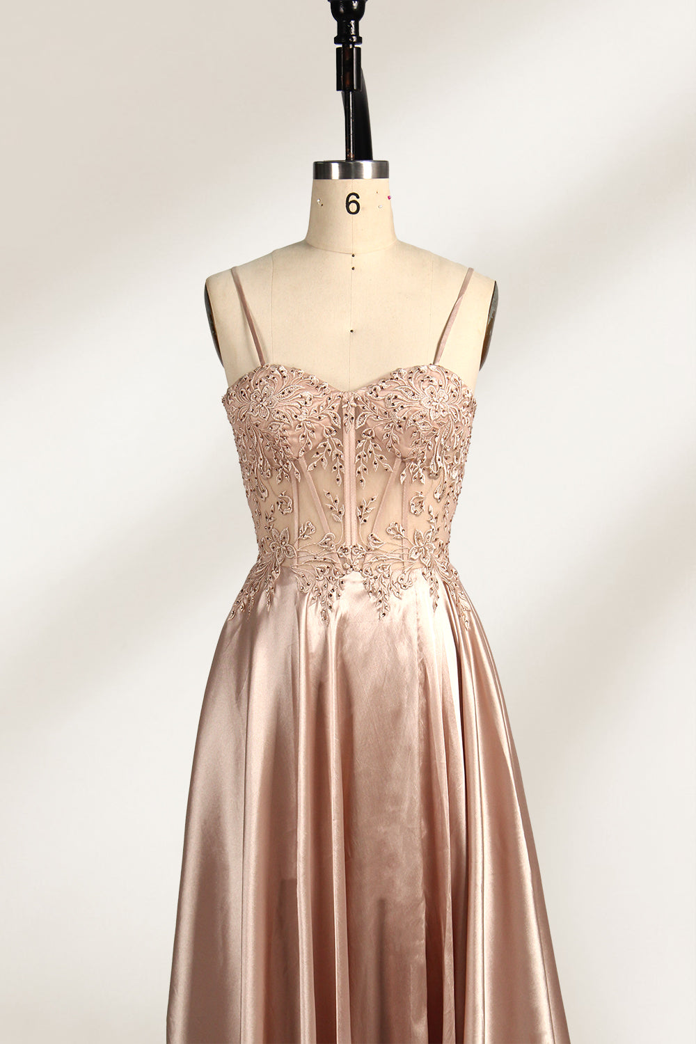 A mannequin showcases a champagne - satin gown. It has thin straps, a sheer lace - detailed bodice, and a voluminous skirt. The elegant design, blending satin and intricate lace, suits formal events like weddings, radiating sophistication.3