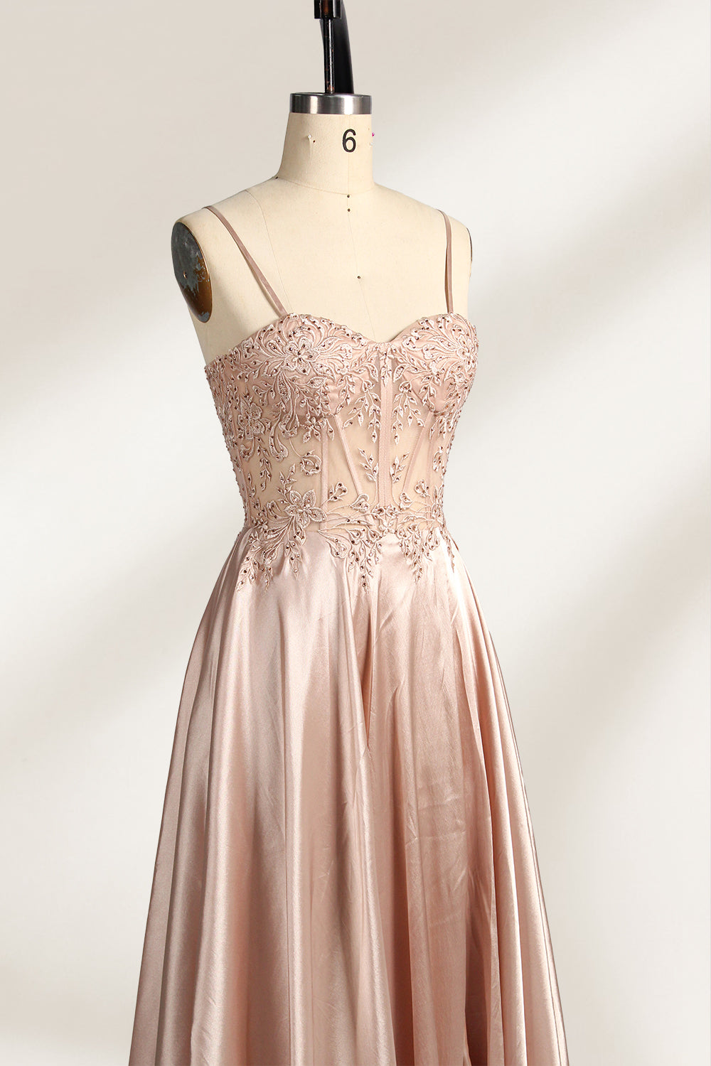 A mannequin showcases a champagne - satin gown. It has thin straps, a sheer lace - detailed bodice, and a voluminous skirt. The elegant design, blending satin and intricate lace, suits formal events like weddings, radiating sophistication.6