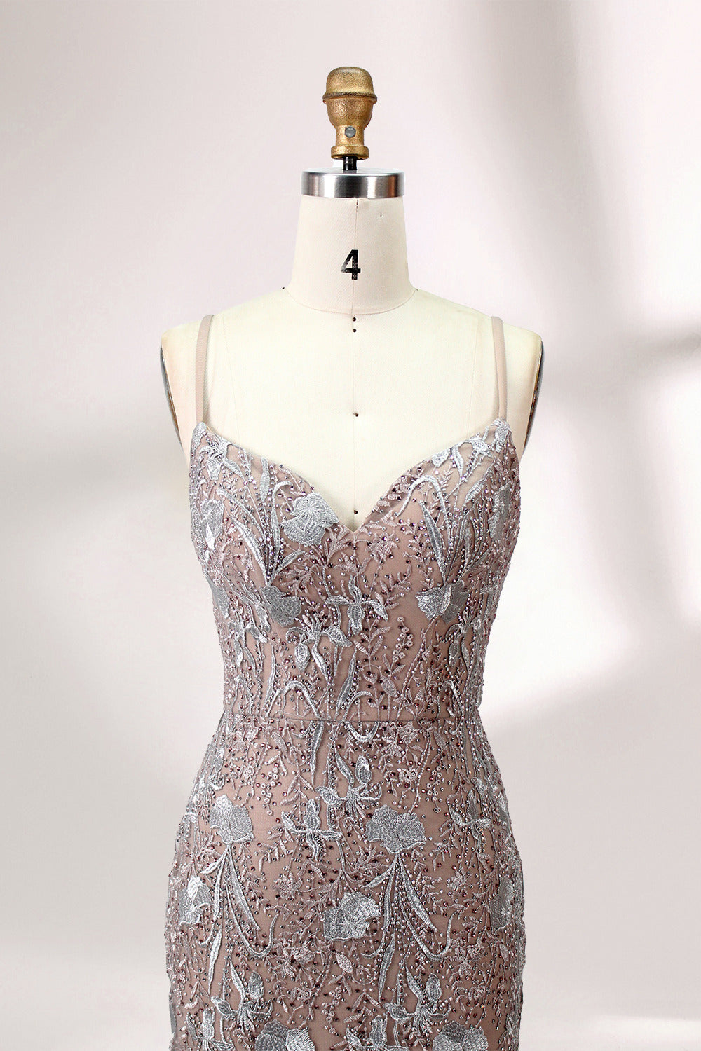 Showcased on a mannequin is a taupe - toned mermaid - cut gown. It has thin straps, a sweetheart neckline, and is embellished with delicate silver floral embroidery all over, plus a flowing tulle skirt. The refined design gives off a glamorous aura, ideal for formal events such as proms or weddings.4