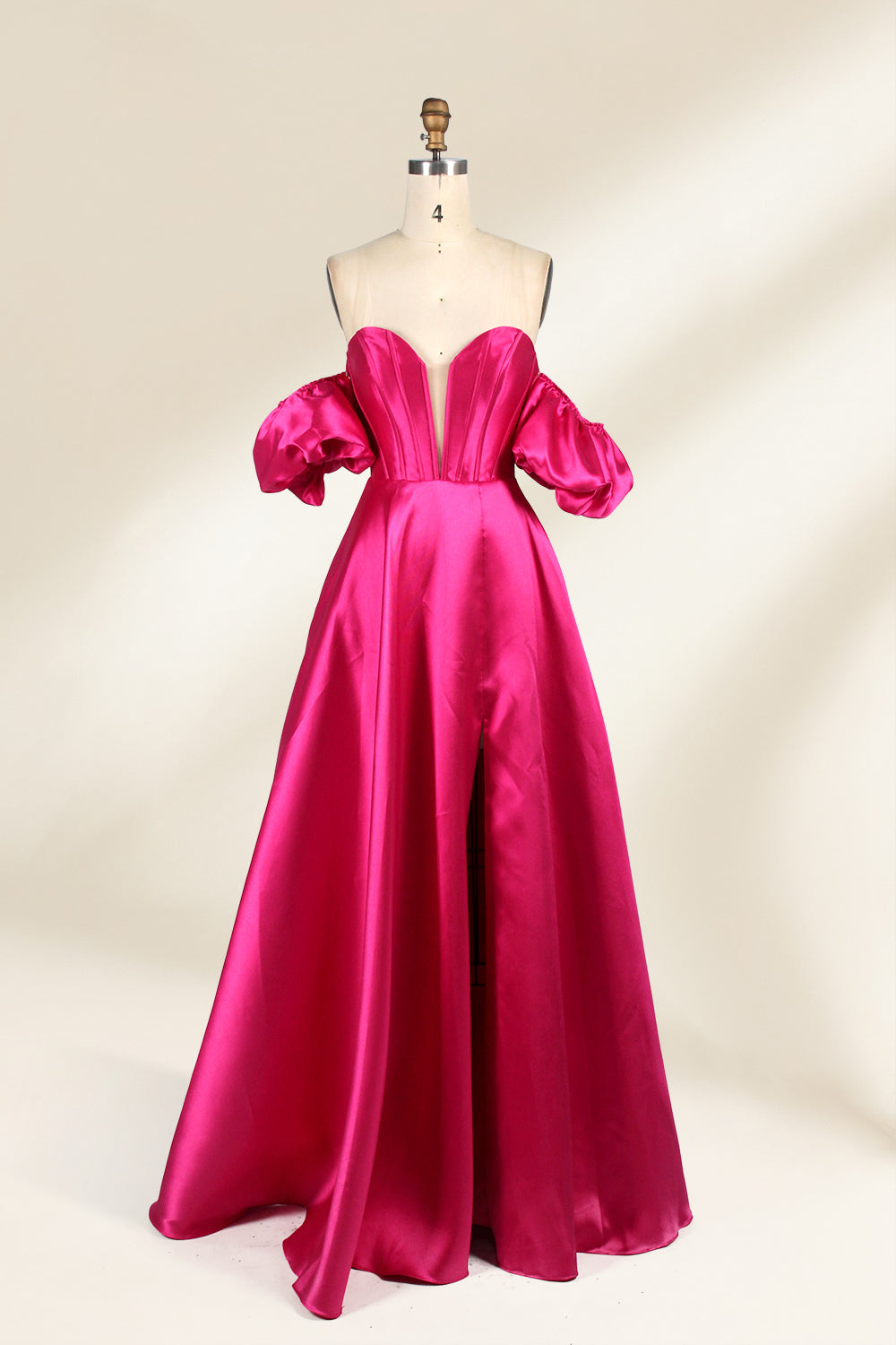 A mannequin showcases a magenta - satin gown. It has an off - the - shoulder, sweetheart neckline, puffed sleeves, and a high side slit. The elegant design, with smooth satin fabric, suits formal events like galas, radiating sophistication.1