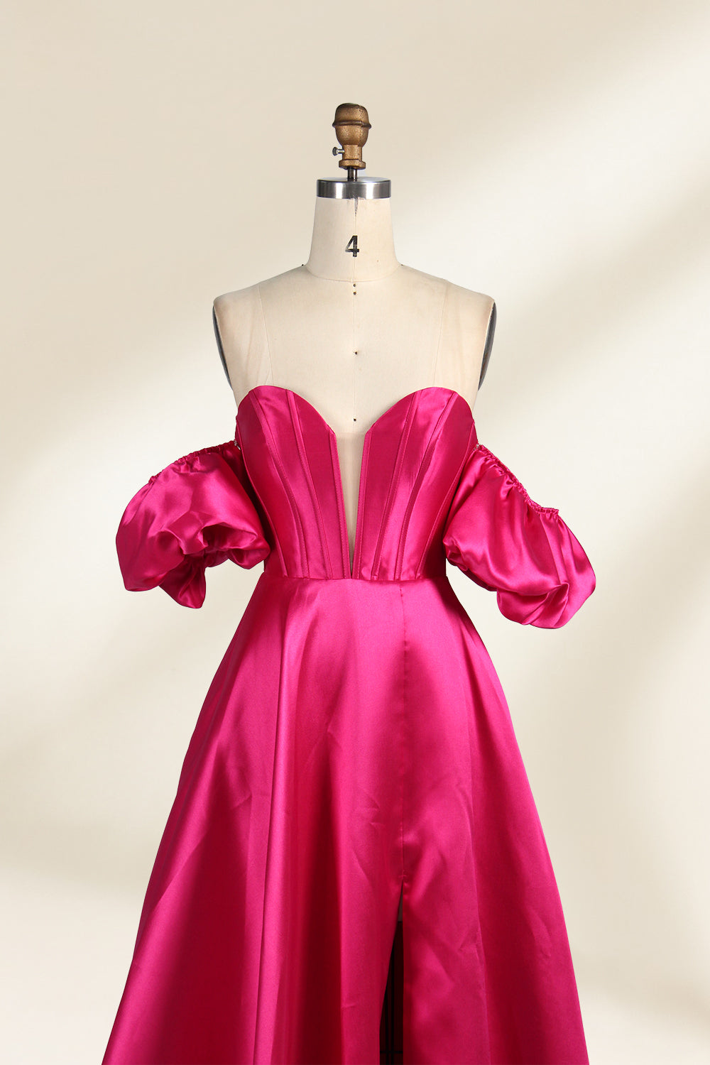 A mannequin showcases a magenta - satin gown. It has an off - the - shoulder, sweetheart neckline, puffed sleeves, and a high side slit. The elegant design, with smooth satin fabric, suits formal events like galas, radiating sophistication.4