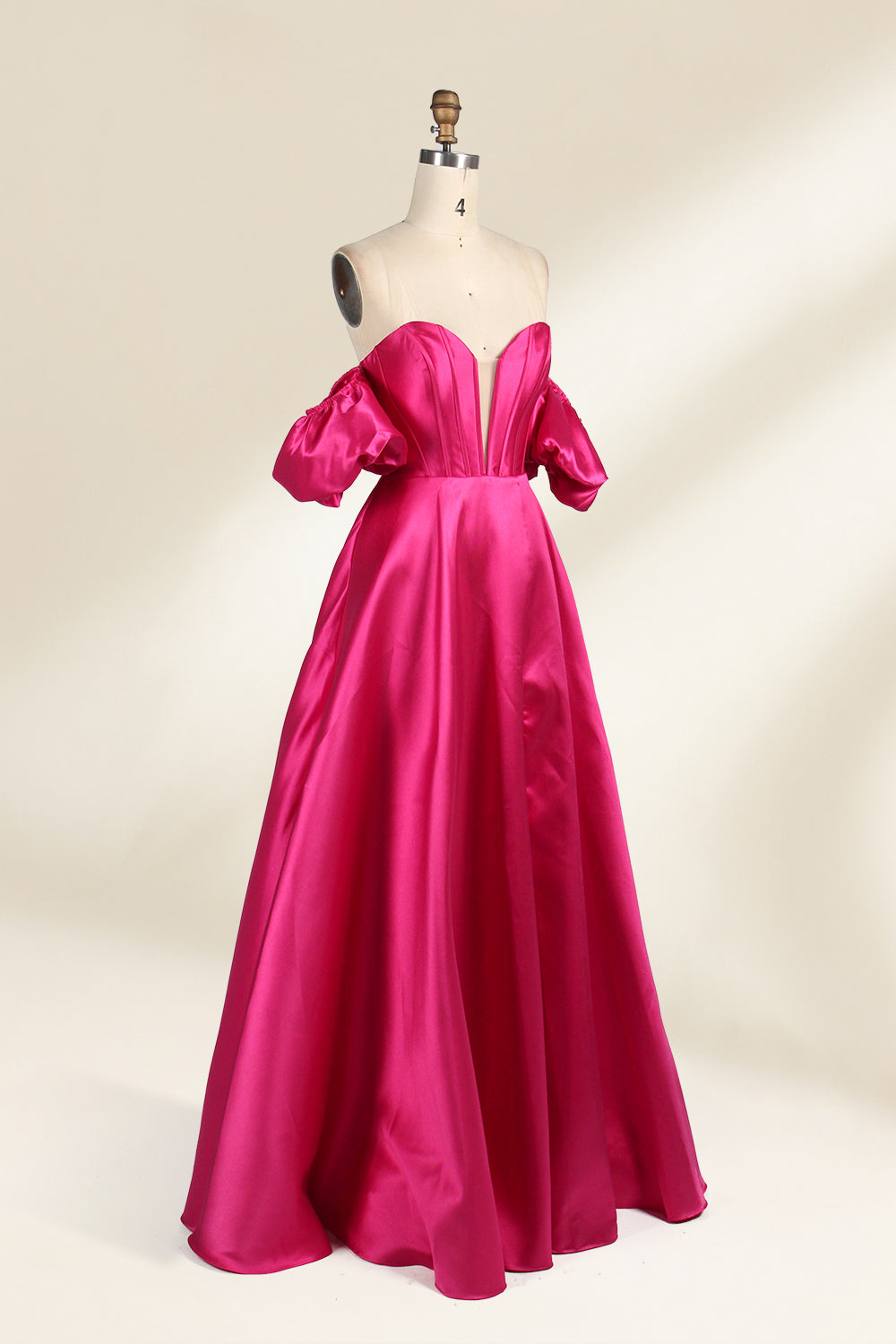 A mannequin showcases a magenta - satin gown. It has an off - the - shoulder, sweetheart neckline, puffed sleeves, and a high side slit. The elegant design, with smooth satin fabric, suits formal events like galas, radiating sophistication.4
