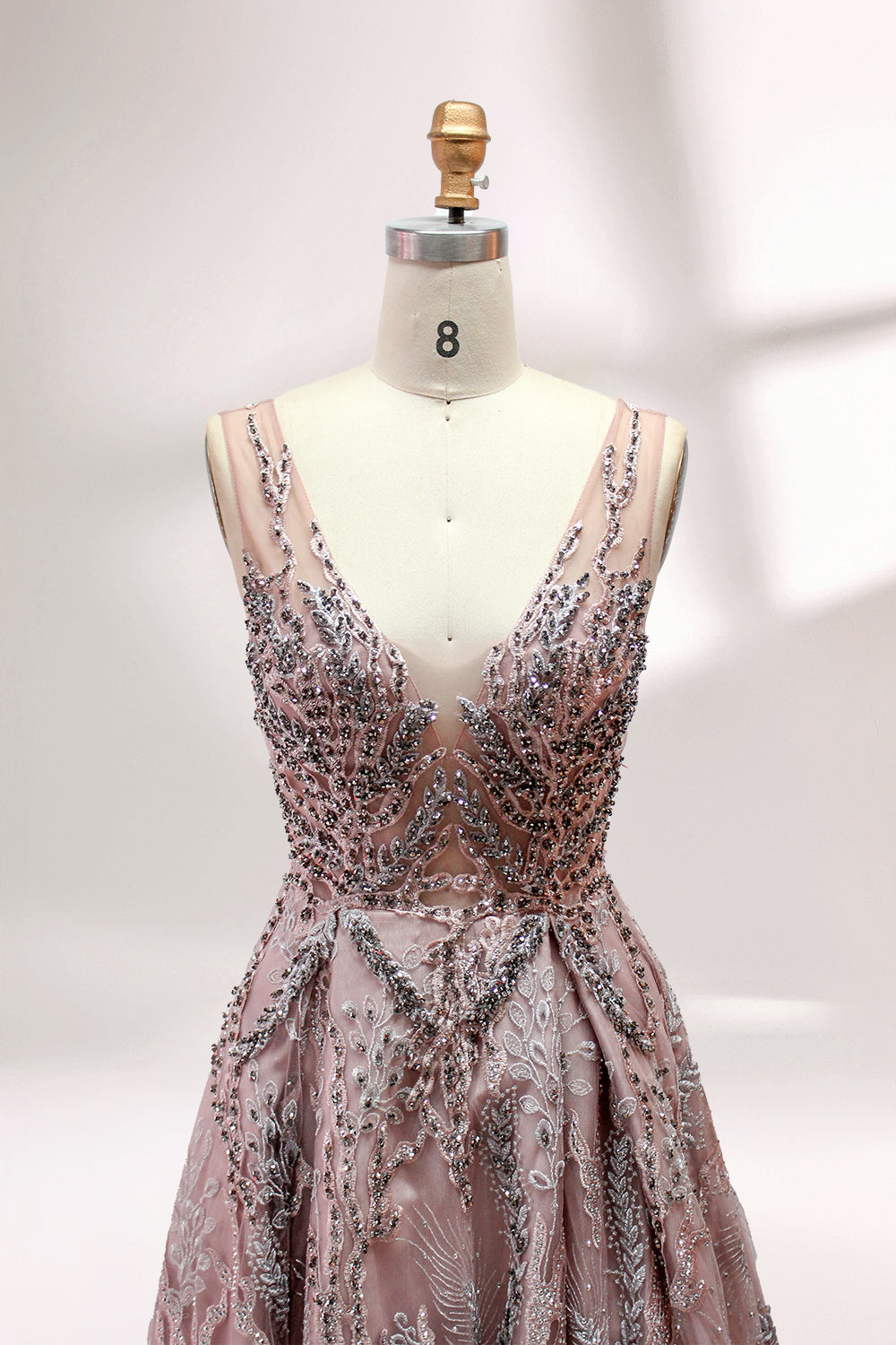 Presented on a mannequin is a mauve evening gown. It features a deep V - neckline, intricate floral embroidery with bead accents, and a flowing skirt. The elegant design creates a romantic and sophisticated look, perfect for formal events.4