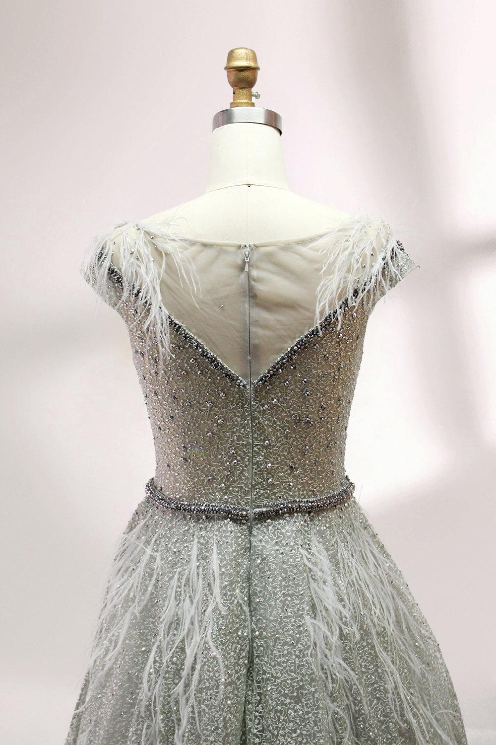 Displayed on a mannequin is a light - green evening gown. It features a sheer neckline with feather and bead embellishments, and a voluminous, glittering skirt. The elegant design creates a dreamy and luxurious look, perfect for formal events.9