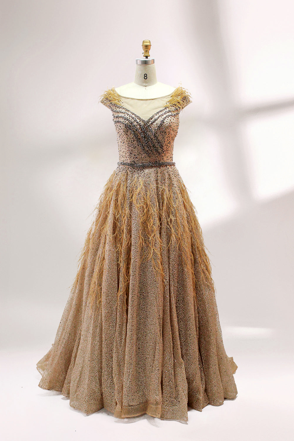 Displayed on a mannequin is a light - green evening gown. It features a sheer neckline with feather and bead embellishments, and a voluminous, glittering skirt. The elegant design creates a dreamy and luxurious look, perfect for formal events.2