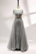 Displayed on a mannequin is a silver - gray evening gown. It features a sheer neckline with fringe details, intricate lace embroidery on the bodice, and a flowing tulle overlay. The elegant design creates a sophisticated and glamorous look, perfect for formal events.1