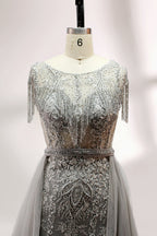 Displayed on a mannequin is a silver - gray evening gown. It features a sheer neckline with fringe details, intricate lace embroidery on the bodice, and a flowing tulle overlay. The elegant design creates a sophisticated and glamorous look, perfect for formal events.4