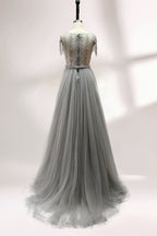Displayed on a mannequin is a silver - gray evening gown. It features a sheer neckline with fringe details, intricate lace embroidery on the bodice, and a flowing tulle overlay. The elegant design creates a sophisticated and glamorous look, perfect for formal events.2