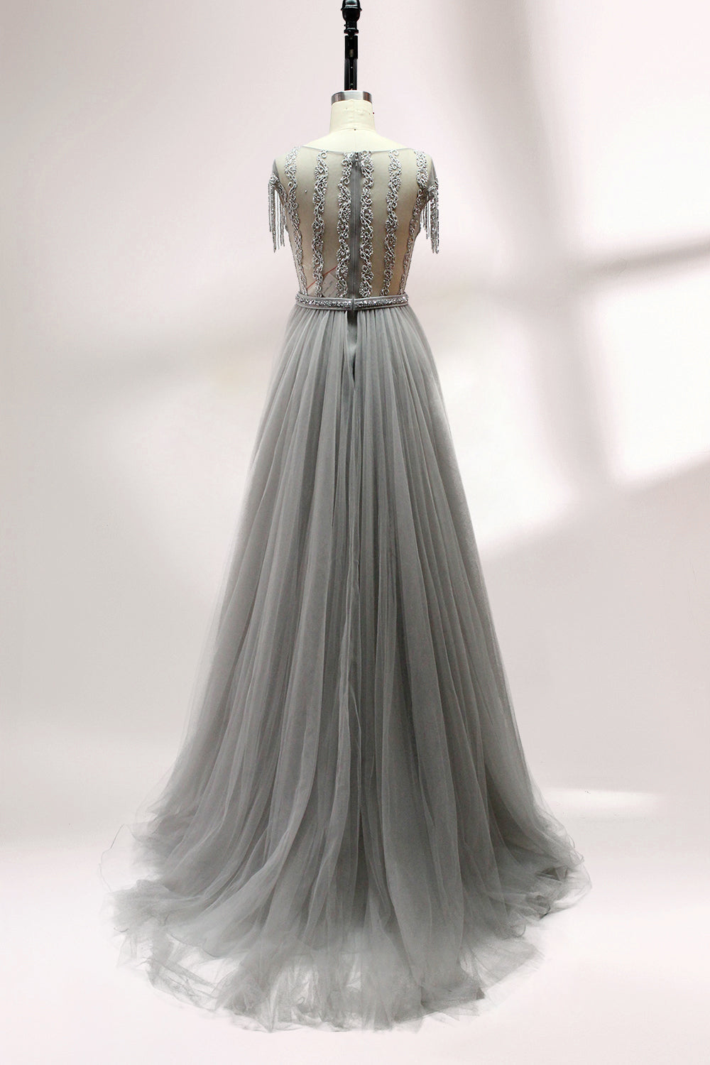 Displayed on a mannequin is a silver - gray evening gown. It features a sheer neckline with fringe details, intricate lace embroidery on the bodice, and a flowing tulle overlay. The elegant design creates a sophisticated and glamorous look, perfect for formal events.2