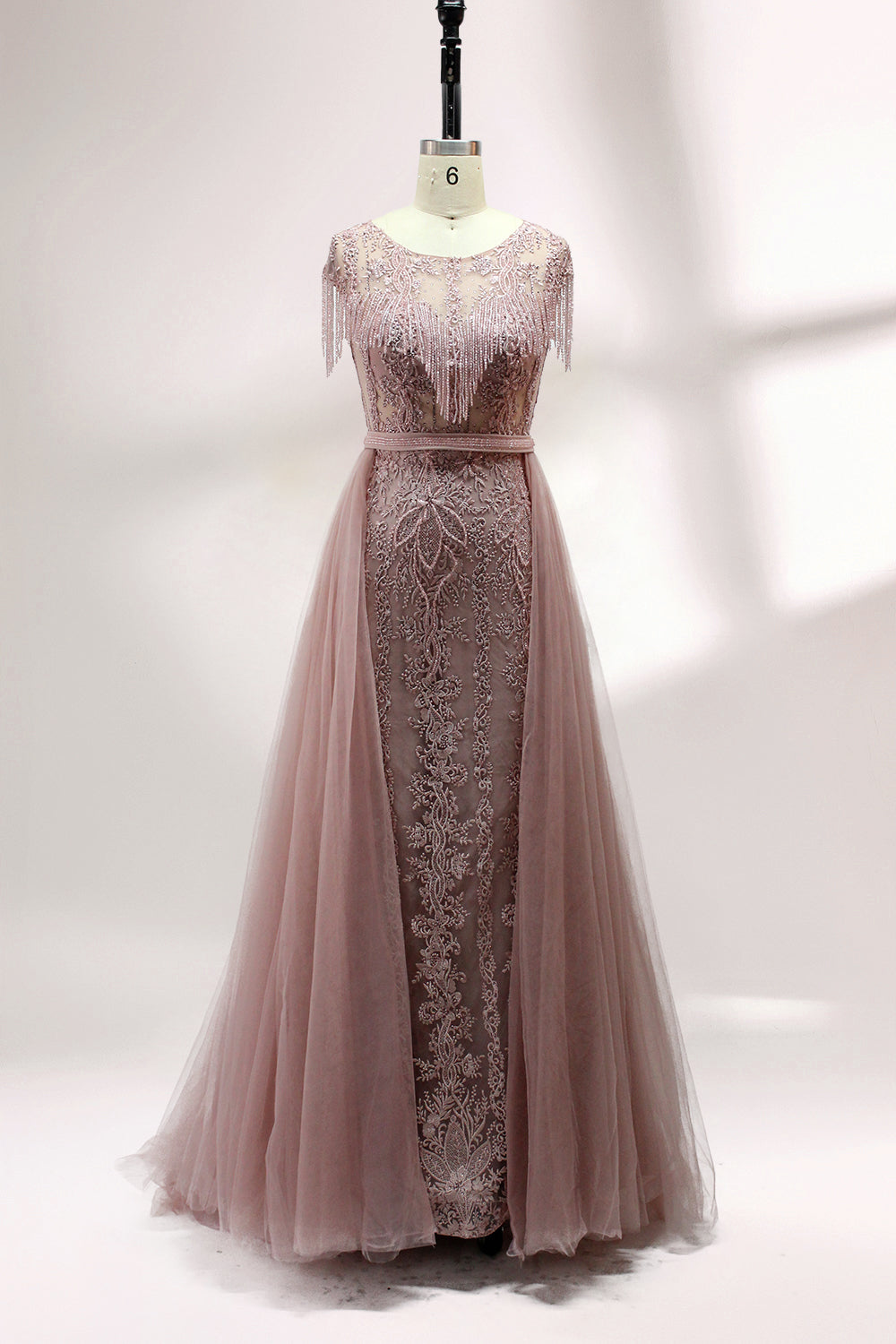 Displayed on a mannequin is a silver - gray evening gown. It features a sheer neckline with fringe details, intricate lace embroidery on the bodice, and a flowing tulle overlay. The elegant design creates a sophisticated and glamorous look, perfect for formal events.3