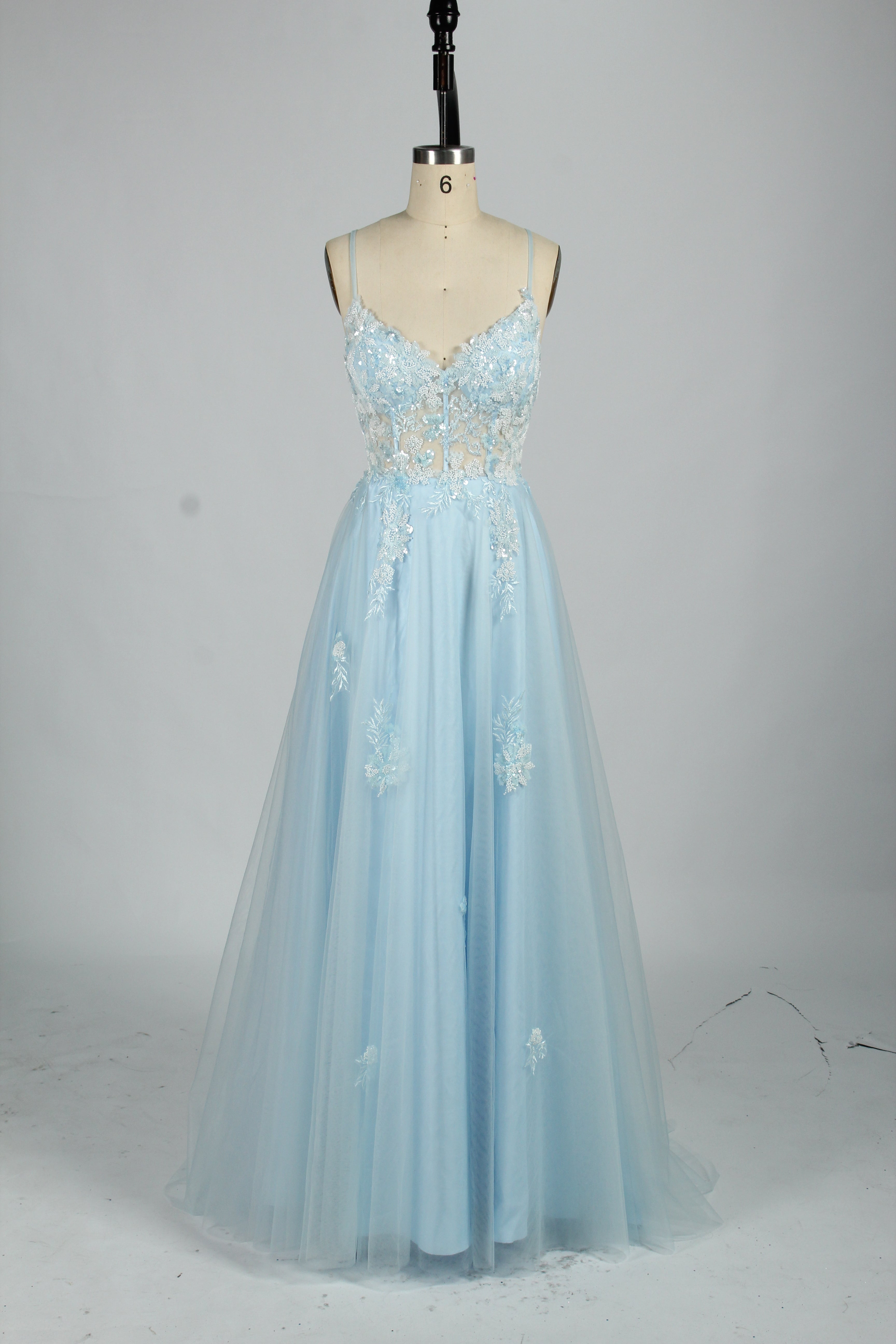 A woman stands against a light background, wearing a blue tulle gown. It features thin straps, a deep V - neckline, intricate floral appliqués with sequins on the bodice, and a high side slit. The voluminous tulle skirt creates a romantic and glamorous look, perfect for formal events like proms or weddings.7