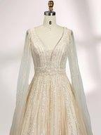 Against a light - hued background, a woman wears an ivory sequin gown with a sheer cape. It features a deep V - neckline, a fitted bodice, and a voluminous skirt. The shimmering sequins and elegant cape design radiate sophistication, perfect for formal events like charity balls, exuding a regal aura.5