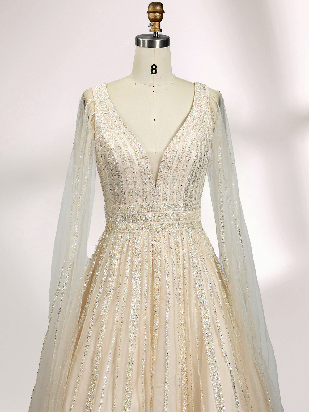 Against a light - hued background, a woman wears an ivory sequin gown with a sheer cape. It features a deep V - neckline, a fitted bodice, and a voluminous skirt. The shimmering sequins and elegant cape design radiate sophistication, perfect for formal events like charity balls, exuding a regal aura.5