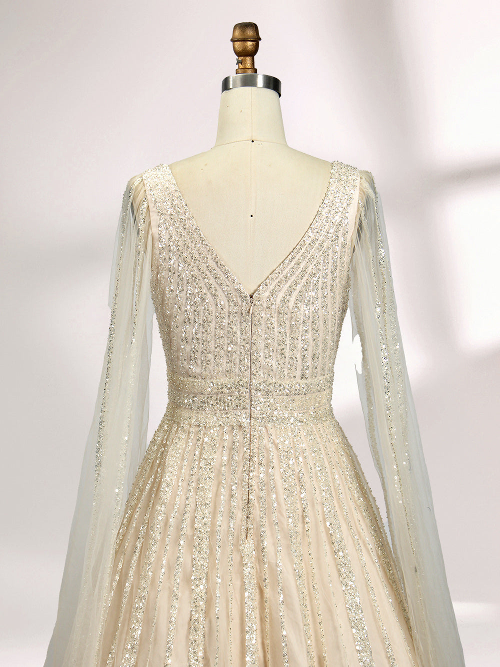 Against a light - hued background, a woman wears an ivory sequin gown with a sheer cape. It features a deep V - neckline, a fitted bodice, and a voluminous skirt. The shimmering sequins and elegant cape design radiate sophistication, perfect for formal events like charity balls, exuding a regal aura.6