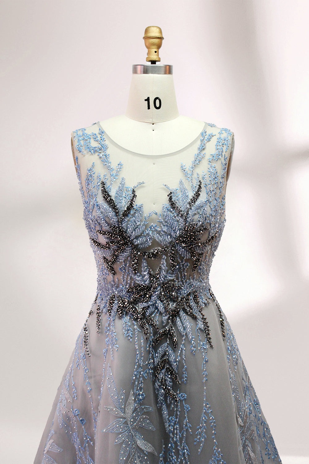 Presented on a mannequin is a gown with a gray base and rich red floral embroidery. It features a sheer neckline, a sleeveless design, and an intricate pattern that gives off a romantic and elegant vibe, perfect for formal events.6