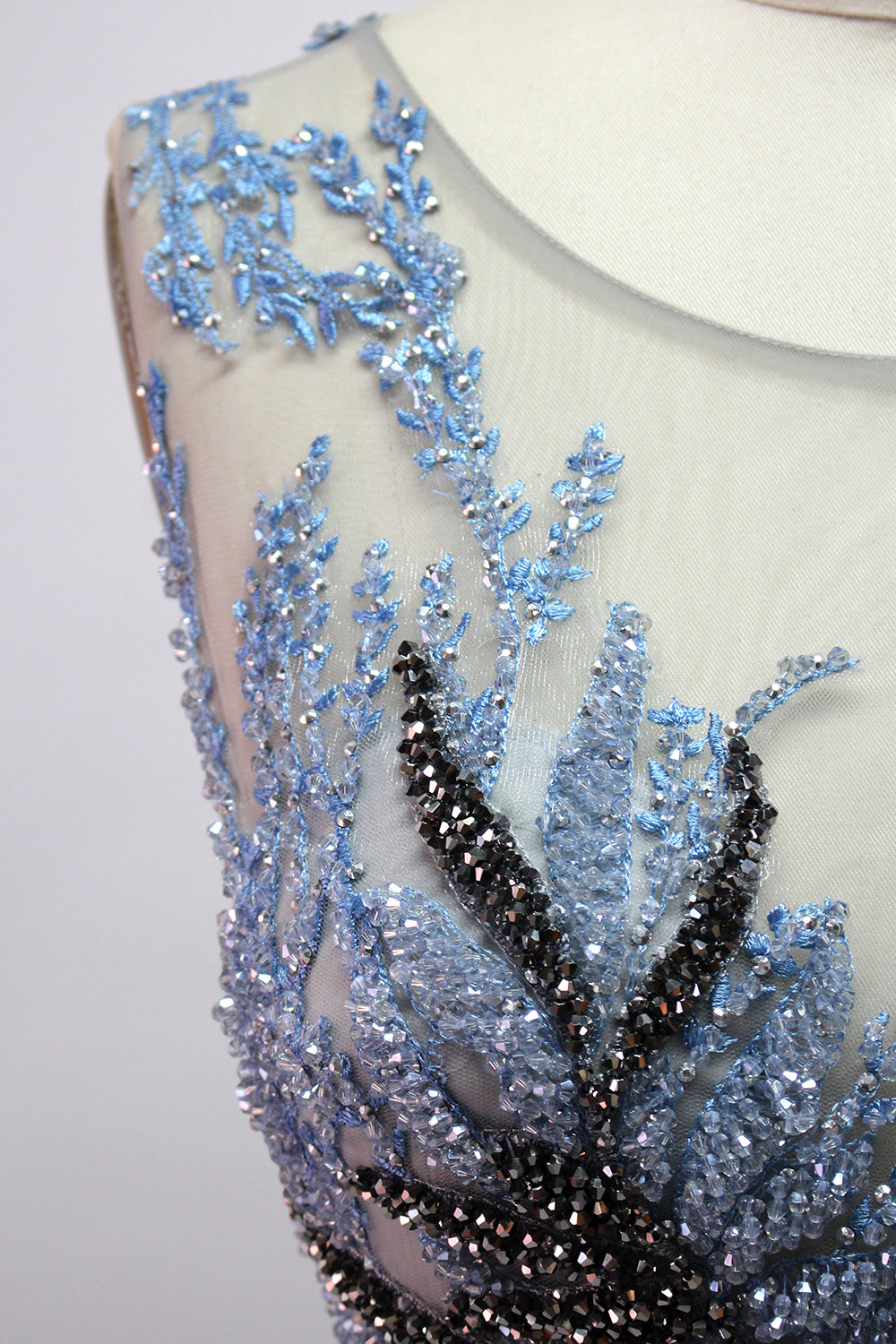 Presented on a mannequin is a gown with a gray base and rich red floral embroidery. It features a sheer neckline, a sleeveless design, and an intricate pattern that gives off a romantic and elegant vibe, perfect for formal events.7