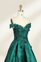 This is a photograph of a stunning, off-the-shoulder, floor-length evening gown displayed on a dress form. The gown is a rich, emerald green satin with intricate black floral lace embroidery on the bodice and hem. The dress features a sweetheart neckline, accentuating the bust, and a fitted waist that flares into a full, flowing skirt. The dress form is beige, with a wooden head and neck, and a metal neck ring. The background is a plain, light cream color, ensuring the dress remains the focal point.04