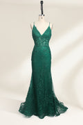 Photograph of a dark green, floor-length evening gown displayed on a white dress form. The gown features a deep V-neckline with thin spaghetti straps, a fitted bodice adorned with intricate lace detailing, and a flowing, slightly flared skirt. The dress showcases a rich, textured fabric with a shimmering effect, accentuating the luxurious and elegant style. The background is a plain, off-white color, ensuring the dress remains the focal point.01