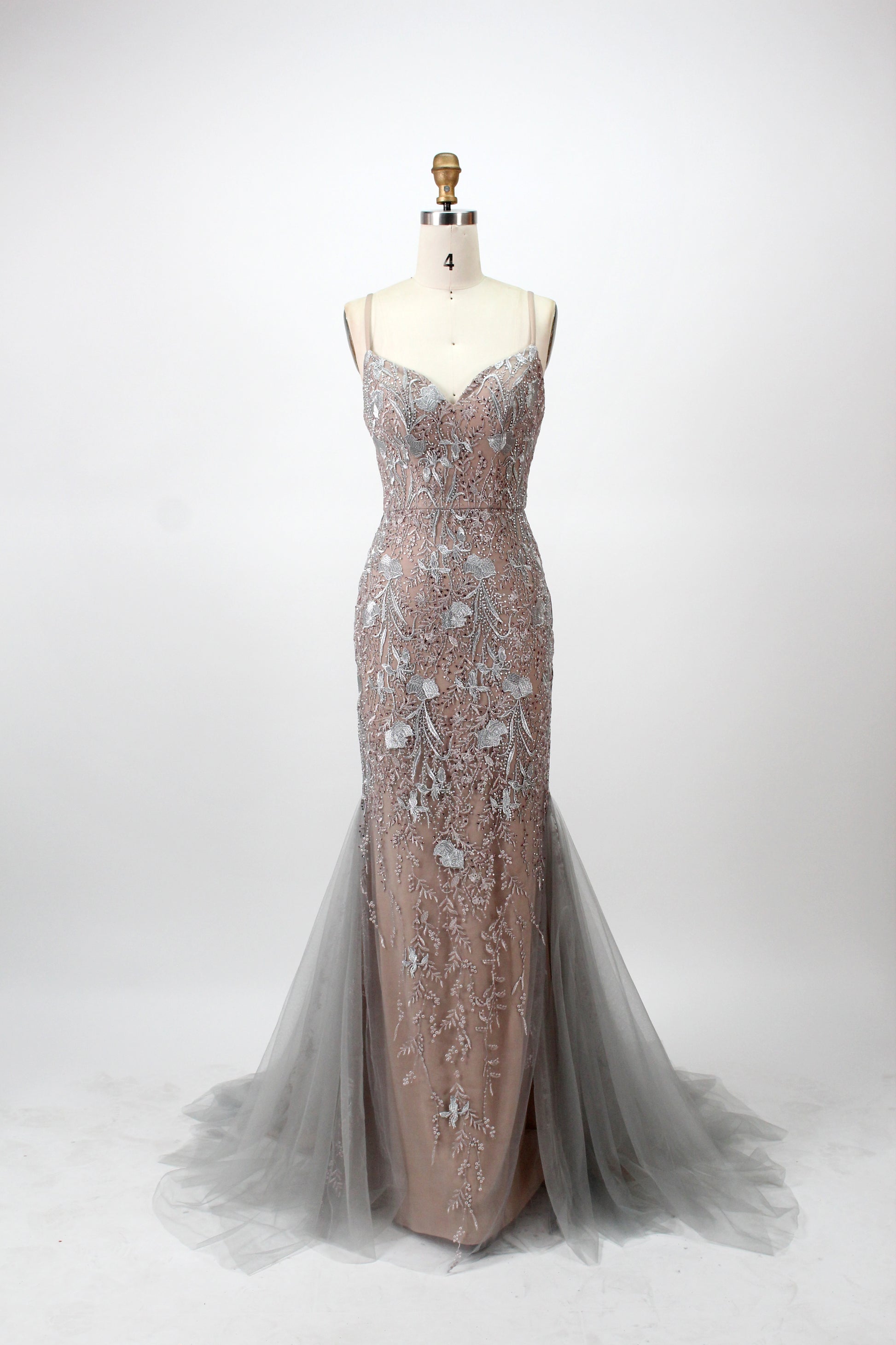photograph of a mannequin, elegant evening gown, floor-length, champagne color, intricate silver floral embroidery, spaghetti straps, fitted bodice, flowing tulle skirt, no shoes, white background, simple studio setting, soft lighting, mannequin headless, fashion design, luxurious fabric, high-end dress, fashion photography, detailed embroidery, sophisticated style, bridal gown, formal wear