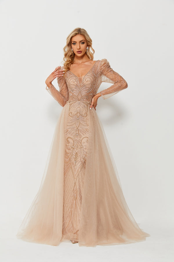 A blonde woman, long wavy hair, standing confidently, hands on hips, wearing a stunning floor-length gown, beige color, intricate beaded embroidery, long sleeves, sheer tulle skirt, elegant and glamorous, white background, studio lighting, high-fashion, model, fashion photography, beautiful, poised, sophisticated, full-length shot, no accessories, minimalist background, no shoes, high-quality image, professional photo shoot, fashion show attire