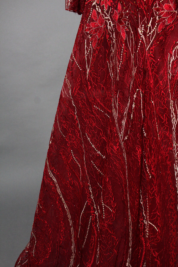 Presented on a mannequin is a deep - red evening gown. It features a sheer neckline, long billowy sleeves, and intricate gold - toned embroidery throughout. The elaborate design gives off a luxurious and elegant vibe, ideal for formal occasions.10