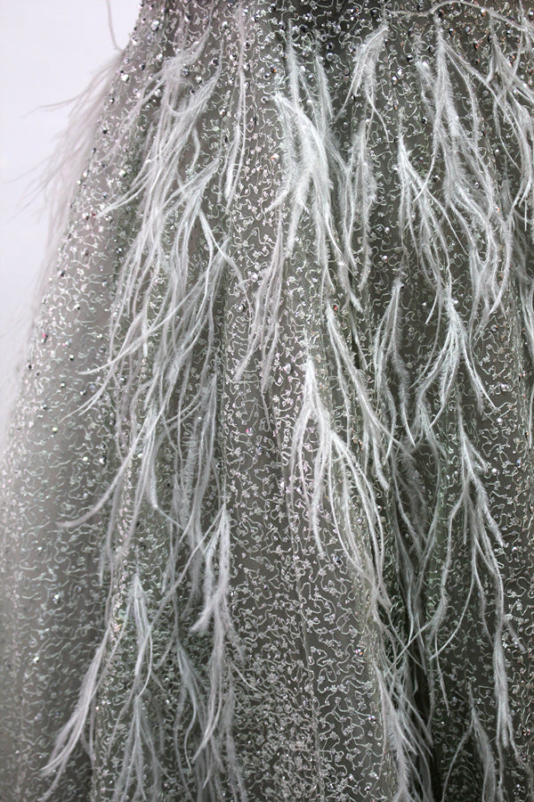 Displayed on a mannequin is a light - green evening gown. It features a sheer neckline with feather and bead embellishments, and a voluminous, glittering skirt. The elegant design creates a dreamy and luxurious look, perfect for formal events.7