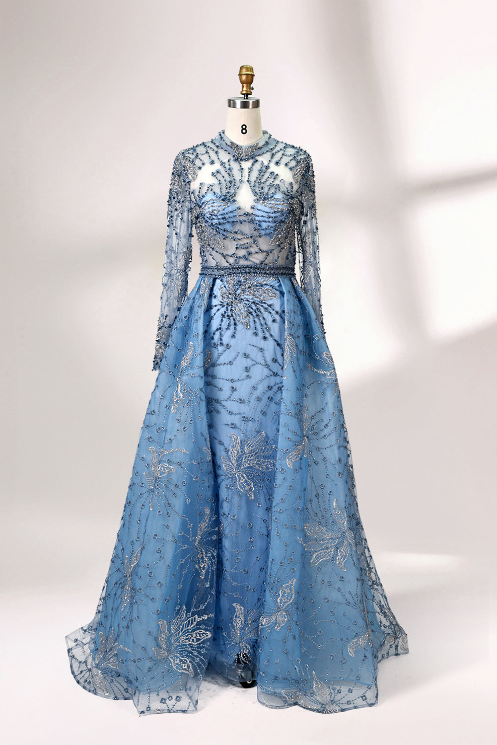 Presented on a mannequin is a blue - toned evening gown. It has a high neckline, long sheer sleeves, and intricate floral embroidery. The elegant design gives off a luxurious and sophisticated vibe, ideal for formal occasions.4