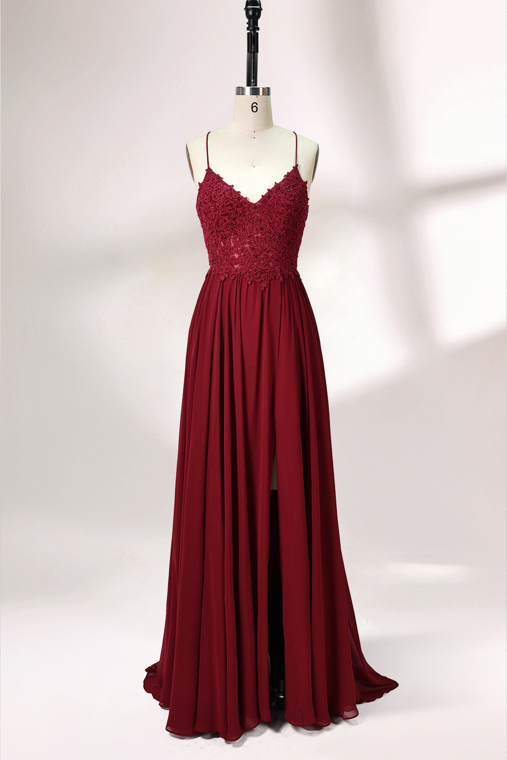 Displayed on a mannequin is a burgundy gown. It features spaghetti straps, a lace - adorned bodice, and a flowing chiffon skirt with a slit. The elegant design suits formal events like galas or weddings.1