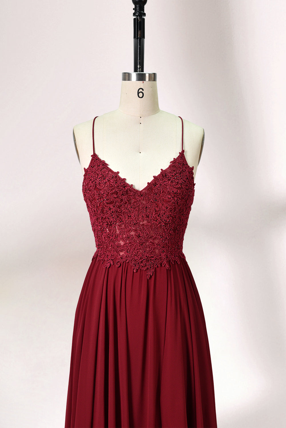 Displayed on a mannequin is a burgundy gown. It features spaghetti straps, a lace - adorned bodice, and a flowing chiffon skirt with a slit. The elegant design suits formal events like galas or weddings.3