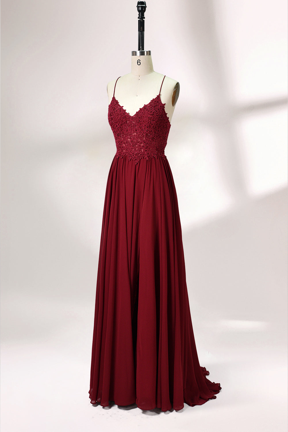 Displayed on a mannequin is a burgundy gown. It features spaghetti straps, a lace - adorned bodice, and a flowing chiffon skirt with a slit. The elegant design suits formal events like galas or weddings.4
