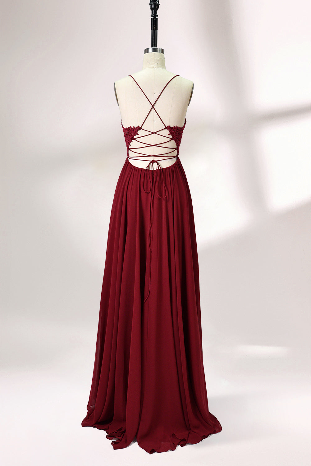 Displayed on a mannequin is a burgundy gown. It features spaghetti straps, a lace - adorned bodice, and a flowing chiffon skirt with a slit. The elegant design suits formal events like galas or weddings.5