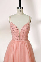 Photograph of a mannequin wearing an elegant, floor-length, blush pink tulle gown with a fitted bodice adorned with sequin embellishments and thin spaghetti straps. The gown has a sweetheart neckline and a full skirt with a subtle sparkle, creating a soft, ethereal effect. The background is a plain white studio setting with soft lighting casting gentle shadows.03