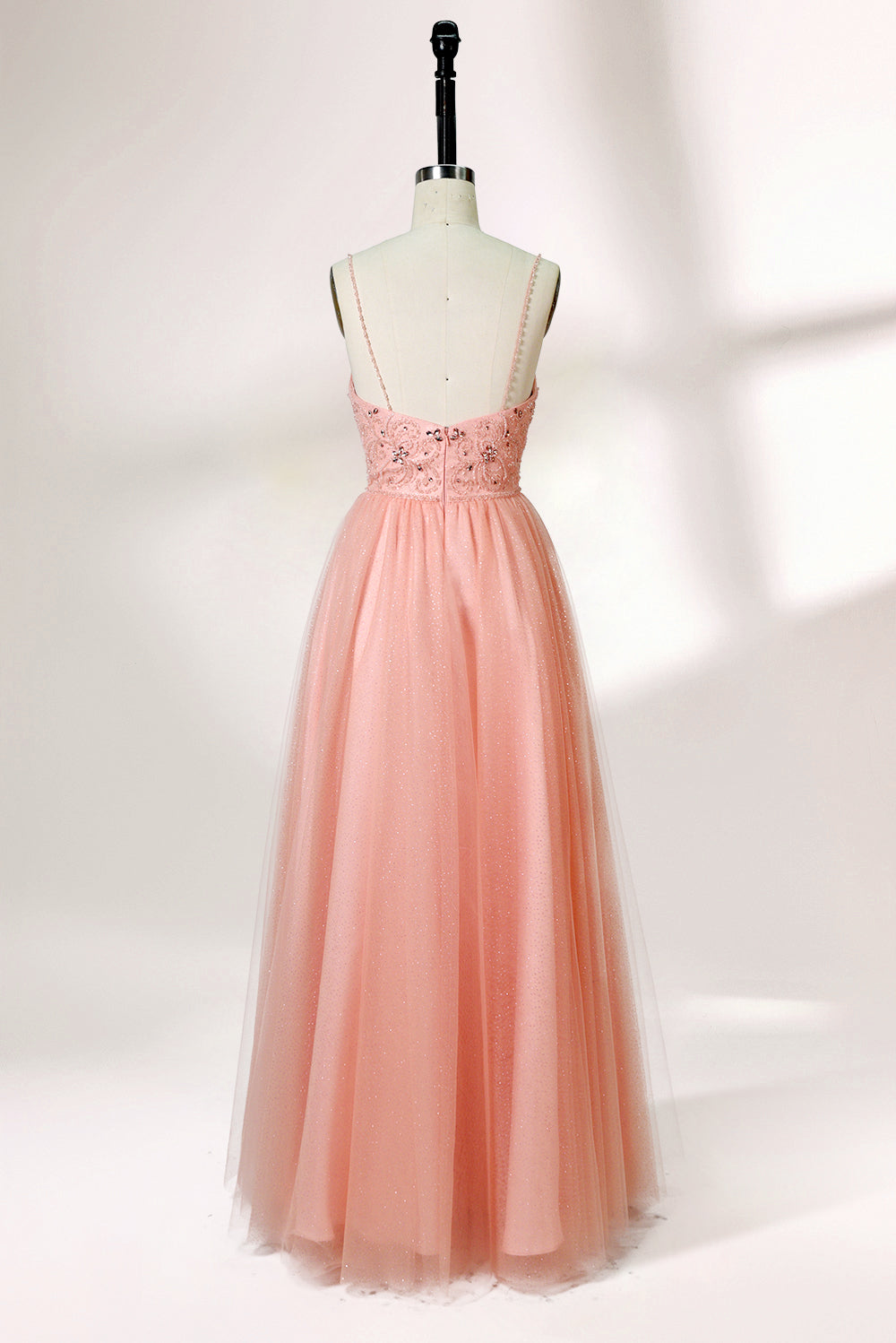 Photograph of a mannequin wearing an elegant, floor-length, blush pink tulle gown with a fitted bodice adorned with sequin embellishments and thin spaghetti straps. The gown has a sweetheart neckline and a full skirt with a subtle sparkle, creating a soft, ethereal effect. The background is a plain white studio setting with soft lighting casting gentle shadows.02