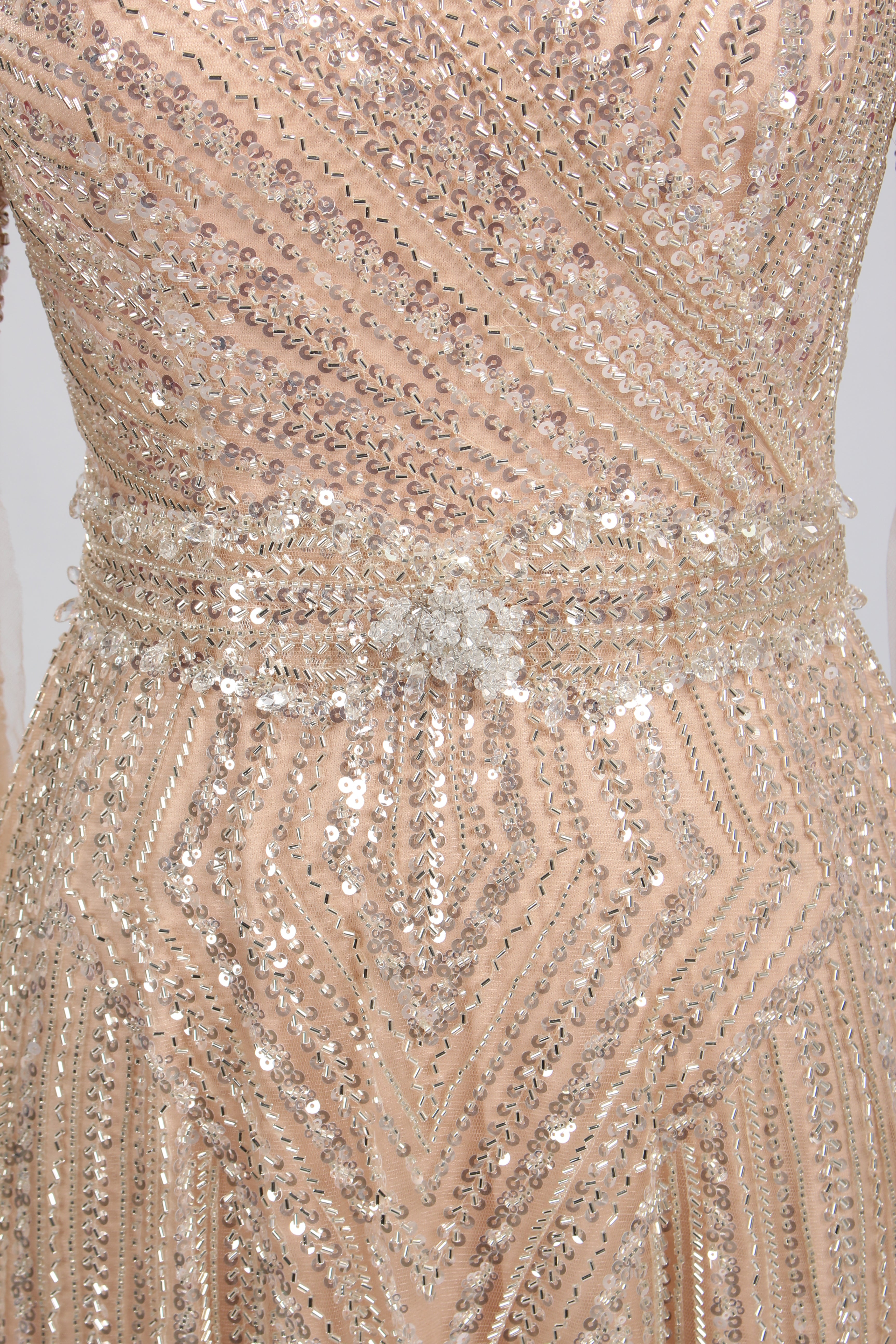 Luxury champagne-colored A-line evening gown on a mannequin, featuring dramatic floor-length cape sleeves, a V-neckline, and shimmering hand-beaded embellishments throughout the tulle fabric.