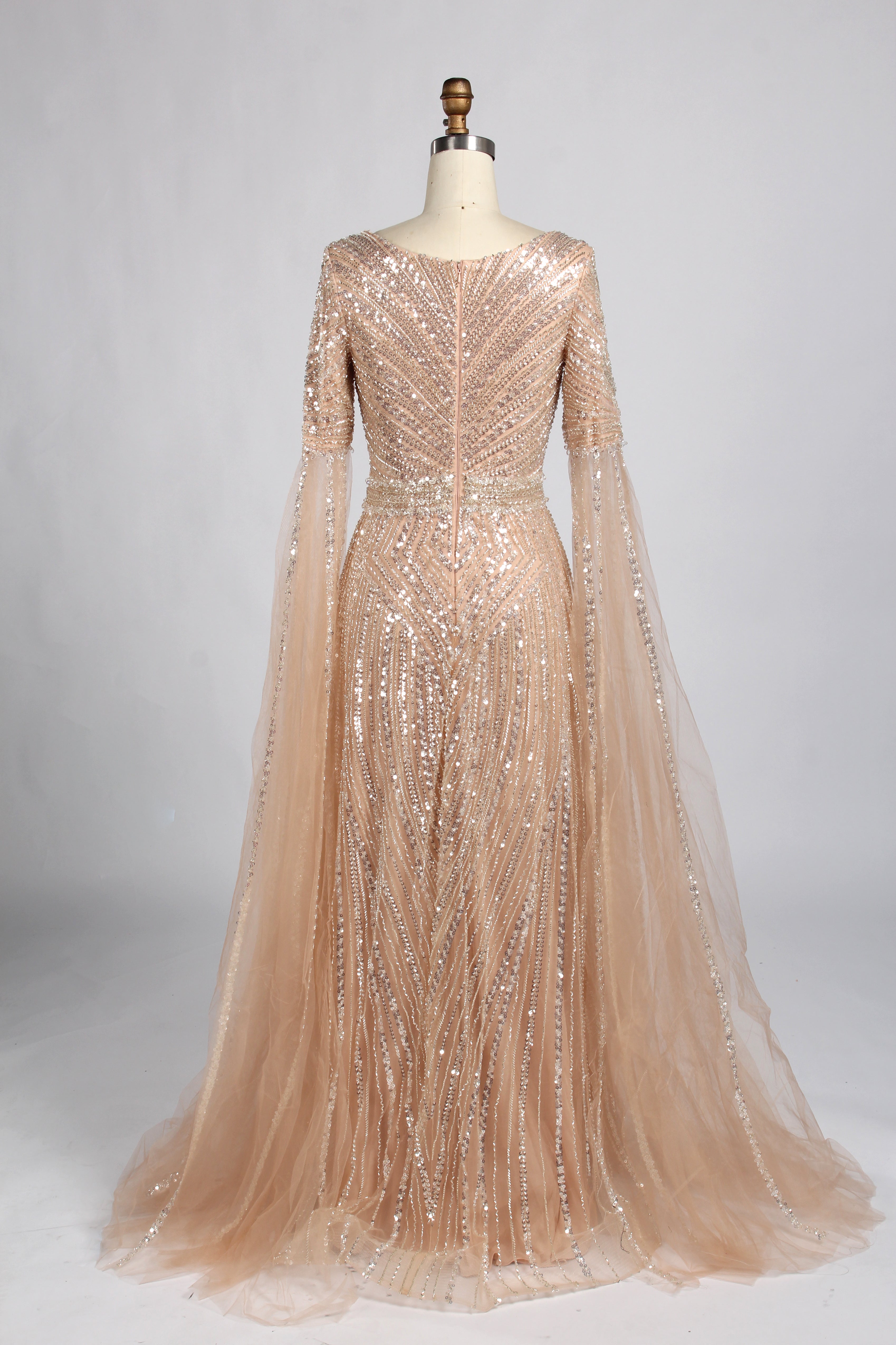 Luxury champagne-colored A-line evening gown on a mannequin, featuring dramatic floor-length cape sleeves, a V-neckline, and shimmering hand-beaded embellishments throughout the tulle fabric.