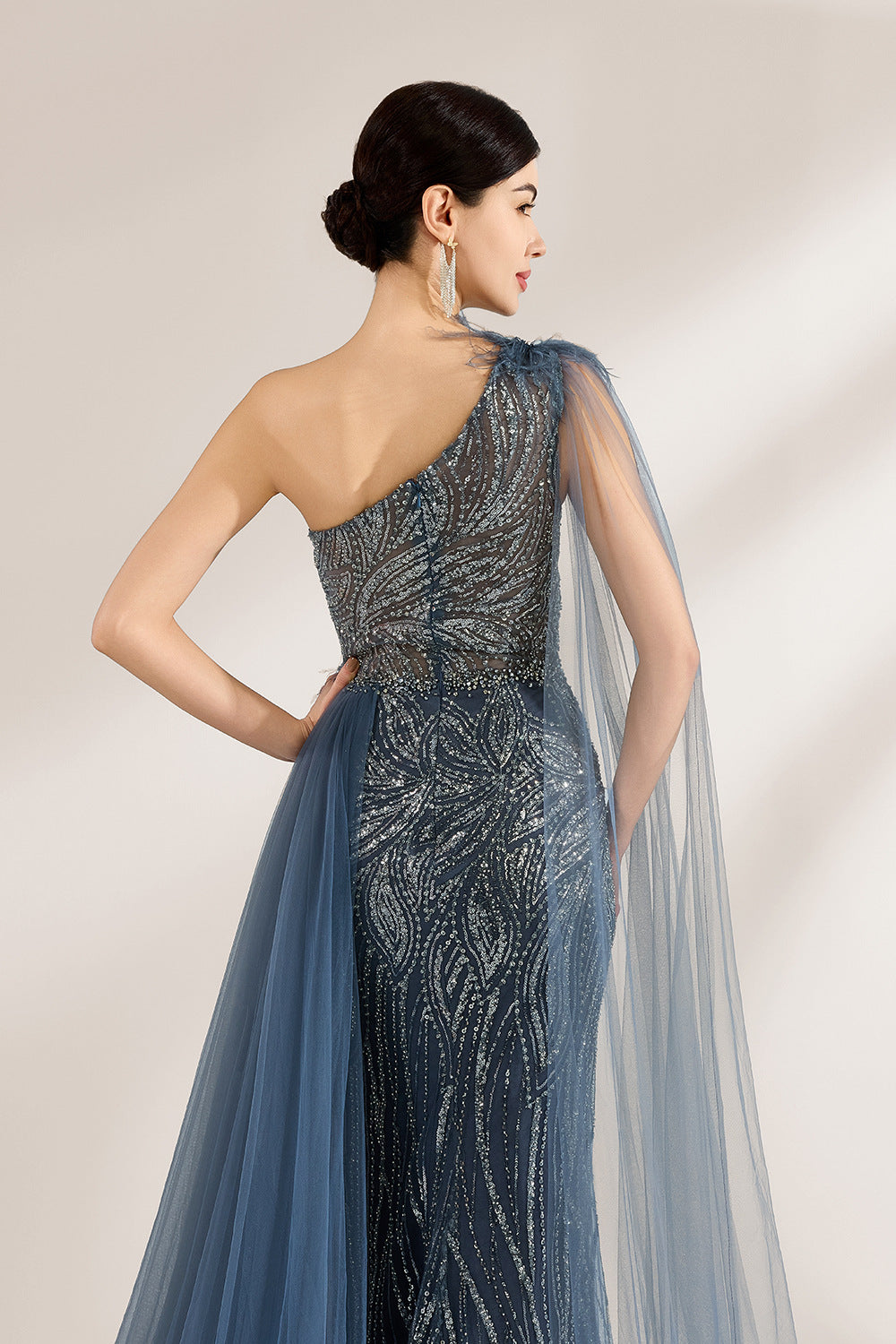 Bathed in soft light, a woman graces the scene in a navy - blue sequined one - shoulder gown. It’s adorned with feather details, a flowing tulle cape, and a high side slit. The mermaid silhouette, shimmering with sequins, exudes opulence, perfect for grand galas or red - carpet moments.5