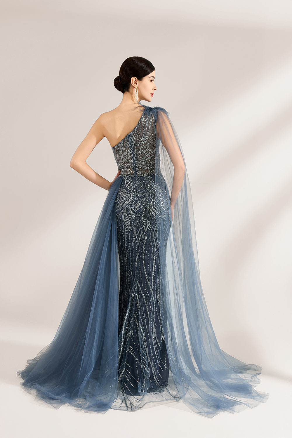 Bathed in soft light, a woman graces the scene in a navy - blue sequined one - shoulder gown. It’s adorned with feather details, a flowing tulle cape, and a high side slit. The mermaid silhouette, shimmering with sequins, exudes opulence, perfect for grand galas or red - carpet moments.4